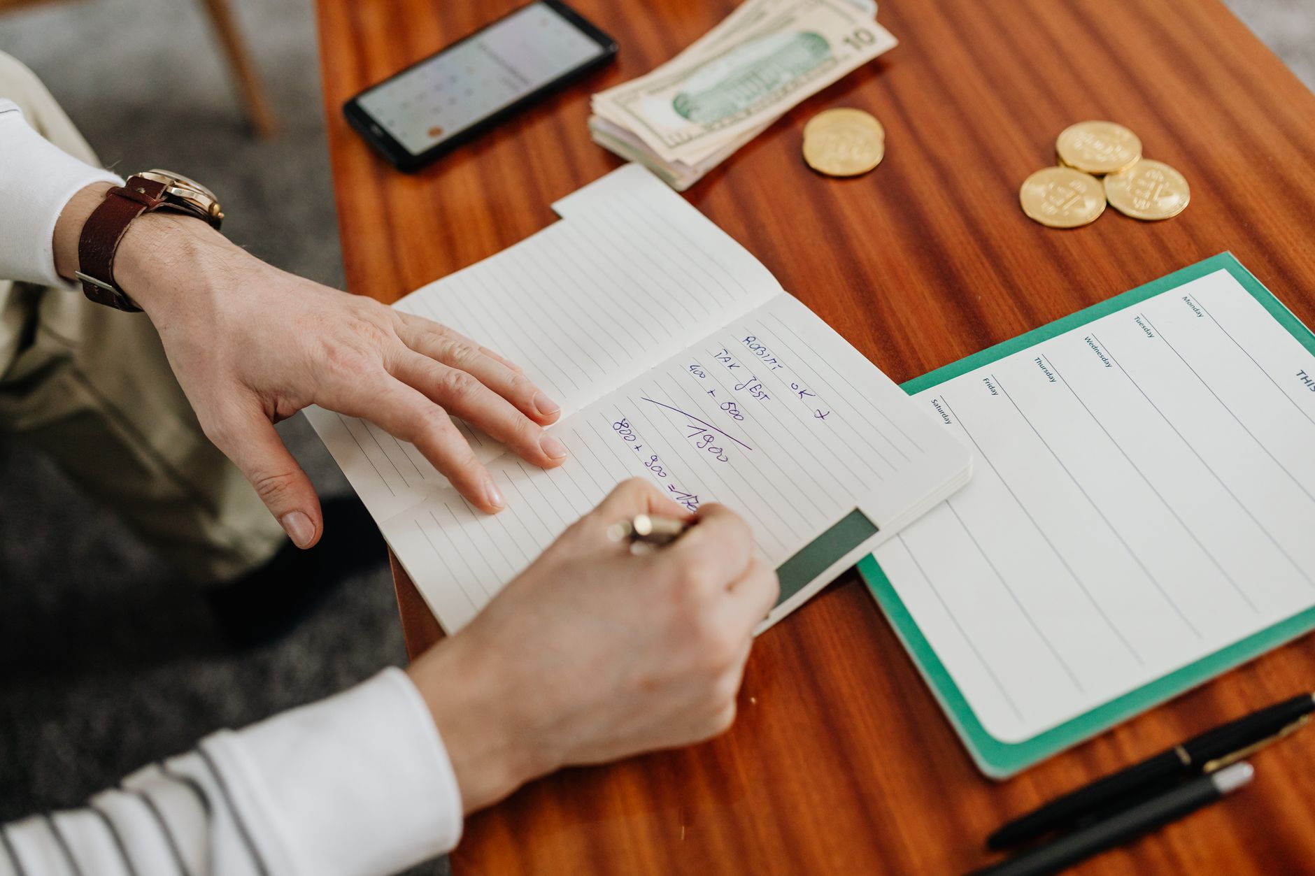 Hands writing financial calculations in a notebook